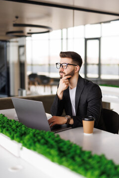 Mmm...I wonder. Handsome young businessman looking thoughtful while working on his laptop in the office.
