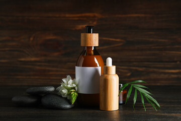 Bottles of cosmetic products, spa stones, palm leaf and flower on dark wooden background