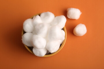Bowl with cotton balls on brown background