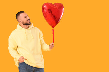 Handsome young happy man with heart-shaped balloon on yellow background
