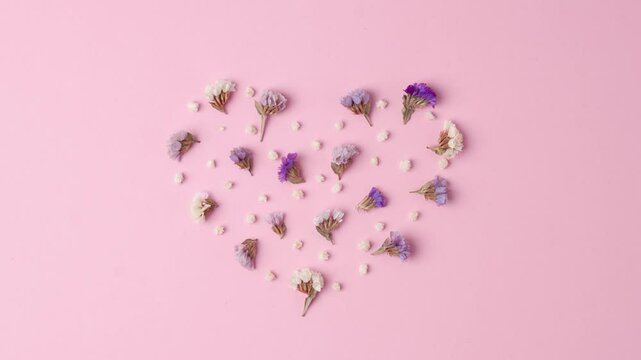 Minimal composition with a heart shape of flowers  on pink background. Flat lay, copy space