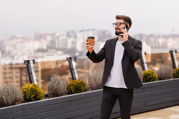 Take a pause. Portrait of smiling businessman drinking coffee on office balcony after talking by phone.