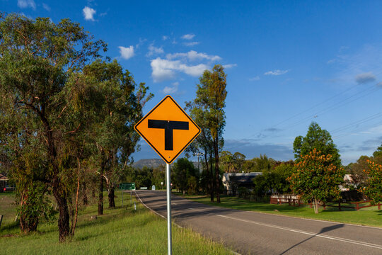 Sunlit t intersection sign beside road in rural village of Broke