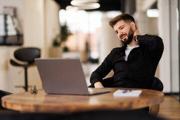 Frustrated young man massaging his nose and keeping eyes closed while sitting at his working place in office