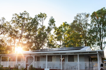 White country cottage with solar panels installed on tin roof with gum trees behind at sunrise