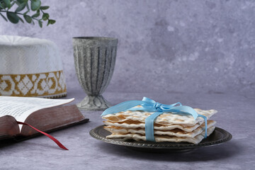 A decorative plate holding neatly stacked matzah tied with a blue ribbon, accompanied by a beautiful old book and a metallic cup in a serene atmosphere. Jewish Passover concept