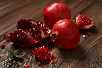 Fresh ripe pomegranates with seeds and leaves on wooden background