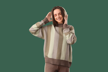 Fototapeta premium Beautiful young woman in stylish sweater and headphones on green background