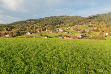 Obraz premium Dispersed settlement on hill slope covered by meadow and forest during beautiful autumn day