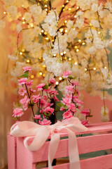 Decorative flowers in a pink box with a bow on the background of a flower tree in the interior