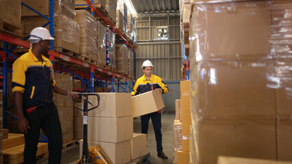 Two warehouse workers are lifting boxes of merchandise on a pallet jack to store on a shelf in a warehouse