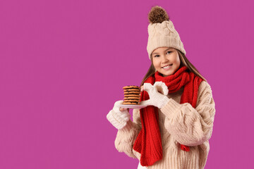 Cute teenage girl in warm clothes holding plate with delicious cookies on pink background