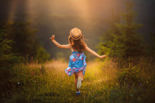 Happy little girl child running playing on the grass at sunset. Warm sunshine around. Hello happy summer concept. Back view, full length.