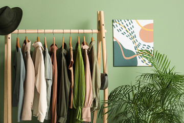 Rack with clothes with stand for shoes and houseplant near green wall