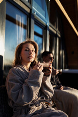 A woman, in a light taupe or beige robe, sits outdoors.