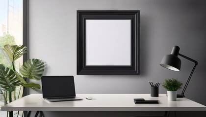 a mockup of an empty black poster frame on the wall sitting above a desk with computer