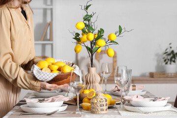 Young woman decorating table setting with bowl of many fresh lemons in dining room, closeup
