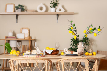 Stylish table setting decorated with many fresh citruses and beautiful lemon tree branches near beige wall in dining room