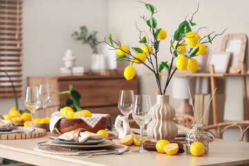 Stylish table setting decorated with many fresh citruses and beautiful lemon tree branches near beige wall in dining room