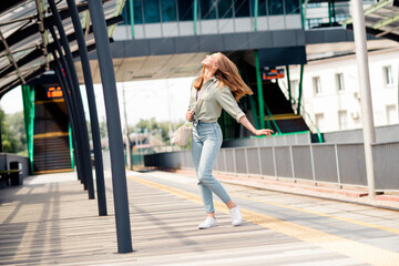 Joyful young woman enjoying a sunny day on a modern urban train platform, embracing the adventure of travel with a carefree spirit