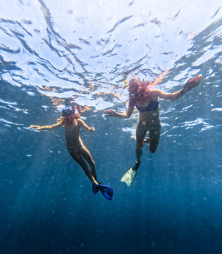 Underwater perspective of Two female snorkelers floating on surface of blue ocean looking down