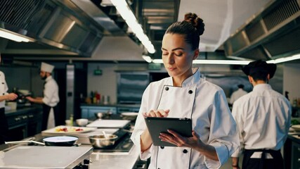 Sous chef managing orders on a tablet in a busy restaurant kitchen