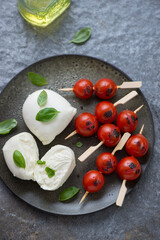 Buffalo mozzarella with grilled cherry tomatoes and basil, vertical shot on a dark-grey granite background, elevated view