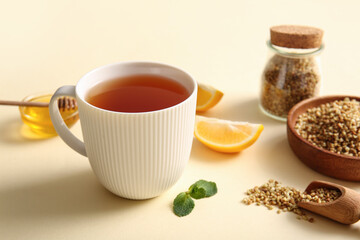 Cup of hot buckwheat tea with lemon and bowl of honey on yellow background