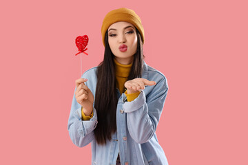 Young woman with paper heart blowing kiss on pink background