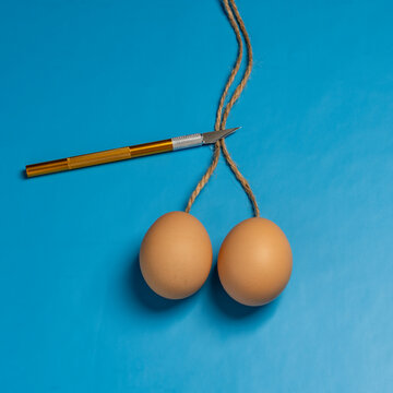 Doctor uses scalpel to cut the rope that holds two eggs on a blue background, closeup. The concept of vasectomy and men's health. Idea about male testicular health