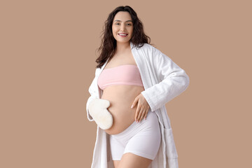 Beautiful young happy pregnant woman with massage mitten on beige background