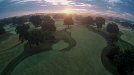 A pristine golf course at sunrise, featuring meticulously maintained grass and turf. The landscape is lush, winding fairways and scattered trees. Sports management. Fisheye effect