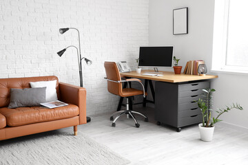 Interior of modern office with leather sofa, lamp and workplace near white brick wall