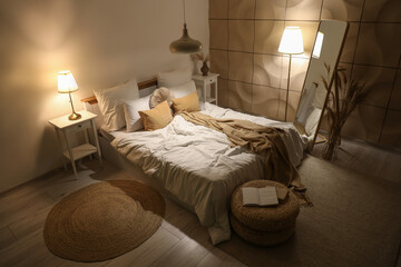 Interior of stylish bedroom with cozy bed, mirror and glowing lamps at night