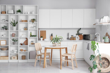 Interior of stylish kitchen with white counters, table, houseplants and shelving unit