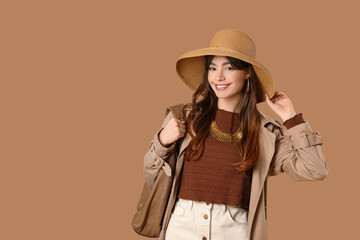 Beautiful young happy fashionable woman in wicker hat with stylish bag on brown background