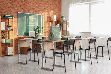 Interior of classroom with backpack on desk and blackboard
