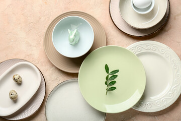 Different clean plates with quail eggs, toy bunny and fresh green leaves on beige background. Easter celebration
