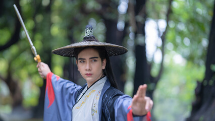 Chinese warriors wearing old traditional costumes. An elegant warrior in a conventional black robe holding a sword wearing a woven bamboo hat in the forest. Ancient Chinese warrior portrait.