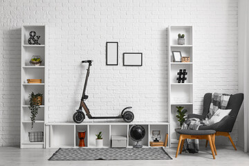 Interior of living room with electric scooter, armchair and shelving units near white brick wall