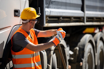 Construction worker wearing safety gear waits by a truck during a sunny day at a worksite