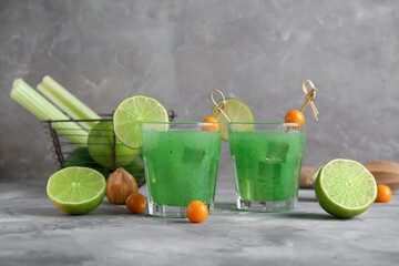 Glasses of green bloody mary cocktail garnished with physalis berries and lime on grey background