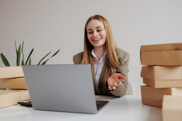 Smiling woman engages in virtual meeting while surrounded by packages in a bright office space