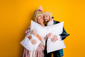 Elegant Couple in Vintage Costumes Holding a Pillow Against Yellow Background