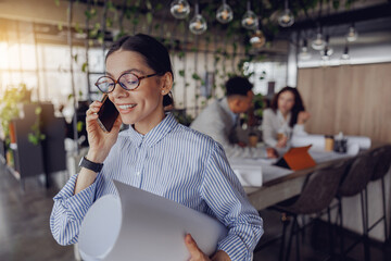 A cheerful and smiling professional engaged in a phone call within a contemporary office environment