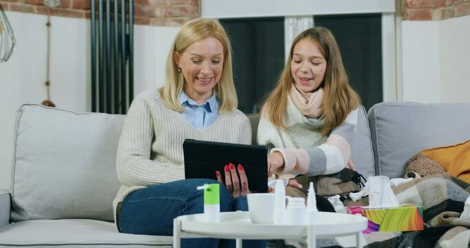Girl putting her head on mother's shoulder while revisioning together funny and intersting movie or video on tablet pc,spending joint leisure at home