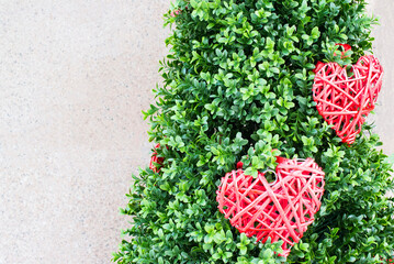 braided red hearts hang on a green shrub