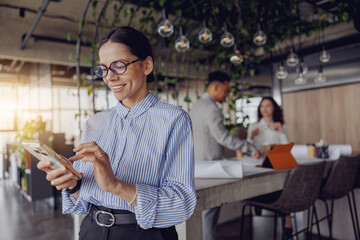 A businesswoman interacts with her smartphone in a stylish office setting, showcasing modern work dynamics.
