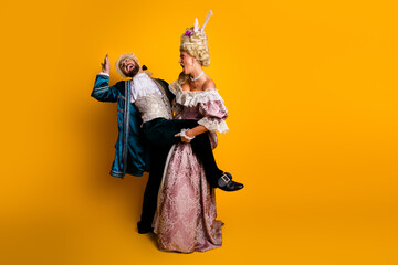 Playful couple dressed in vintage costumes posing against a bright yellow background, evoking a mix...