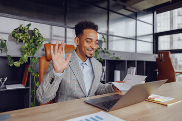 A cheerful man smiling brightly and waving enthusiastically during a virtual meeting set in a...